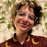 photograph of yasmine, with short curly hair, glasses, and a maroon shirt.